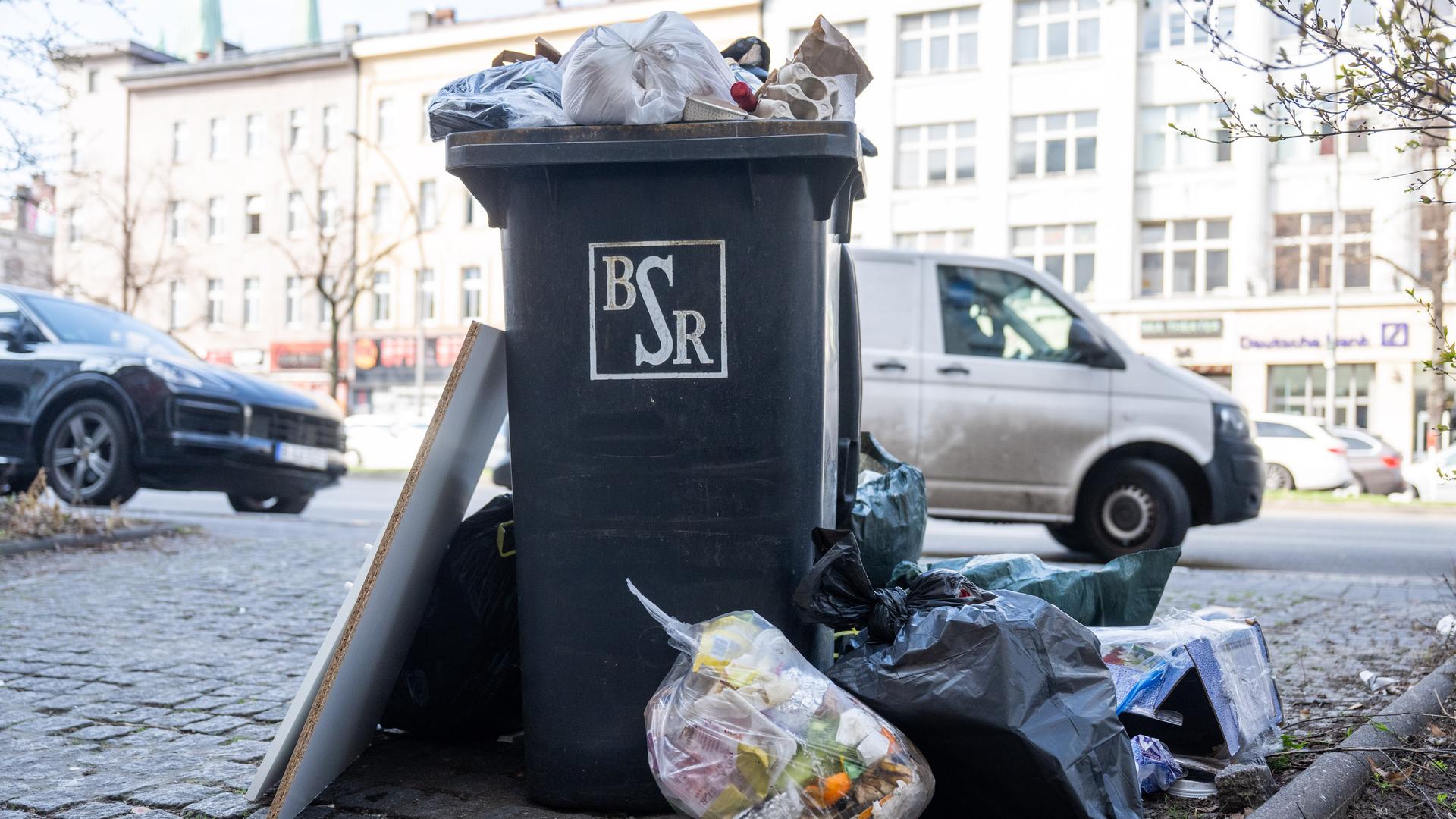 Eine nicht geleerte Mülltonne mit Hausmüll steht vor einem Mehrfamilienhaus. Anfang der Woche startete der Warnstreik bei der Berliner Stadtreinigung und die Mülltonnen werden nicht geleert.