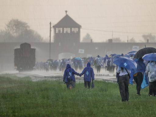 Das ehemalige Konzentrationslager Ausschwitz wird von heftigem Niederschlag heimgesucht. Auf dem Bild sind mehrere junge Leute zu sehen, die dem KZ einen Besuch abstatten. 