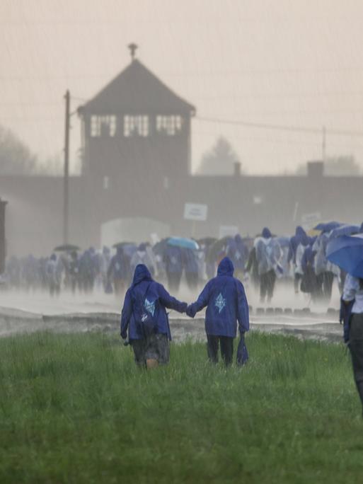 Das ehemalige Konzentrationslager Ausschwitz wird von heftigem Niederschlag heimgesucht. Auf dem Bild sind mehrere junge Leute zu sehen, die dem KZ einen Besuch abstatten. 