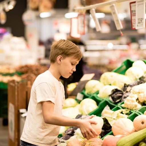 Ein Junge steht beim Gemüse im Supermarkt und hält einen Kürbis in den Händen.
