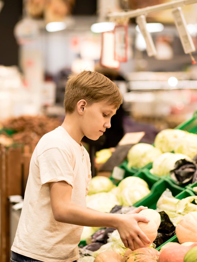Ein Junge steht beim Gemüse im Supermarkt und hält einen Kürbis in den Händen.