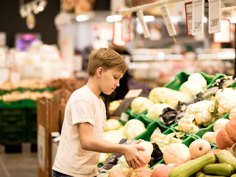 Ein Junge steht beim Gemüse im Supermarkt und hält einen Kürbis in den Händen.