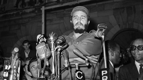 Eine historische scharz-weiß Aufnahme zeigt Fidel Castro angeblitzt vor Mikrofonen am 13. März 1959 vorm Präsidentenpalast in Havanna bei einer Gedenkveranstaltung für die Revolutionäre, die beim Angriff auf den Präsidentenpalast getötet wurden. Der Anschlag wurde von Mitgliedern des Directorio Revolucionario verübt, einer Gruppe, die hauptsächlich aus Universitätsstudenten bestand. Das Directorio arbeitete mit der Bewegung des 26. Juli und anderen revolutionären Gruppen zusammen, um das Batista-Regime zu stürzen.