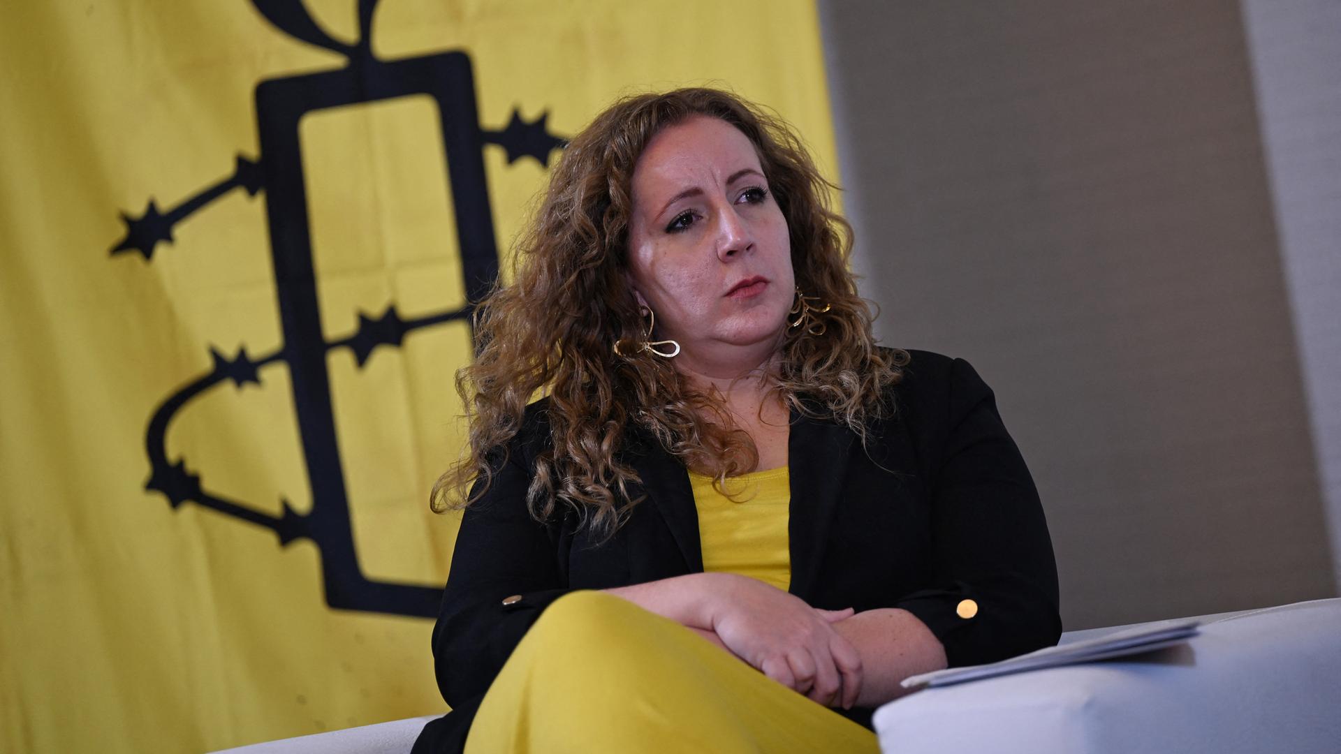 Valentina Ballesta sitzt in einem Sessel. Im Hintergrund das gelb-schware Logo von Amnesty International.