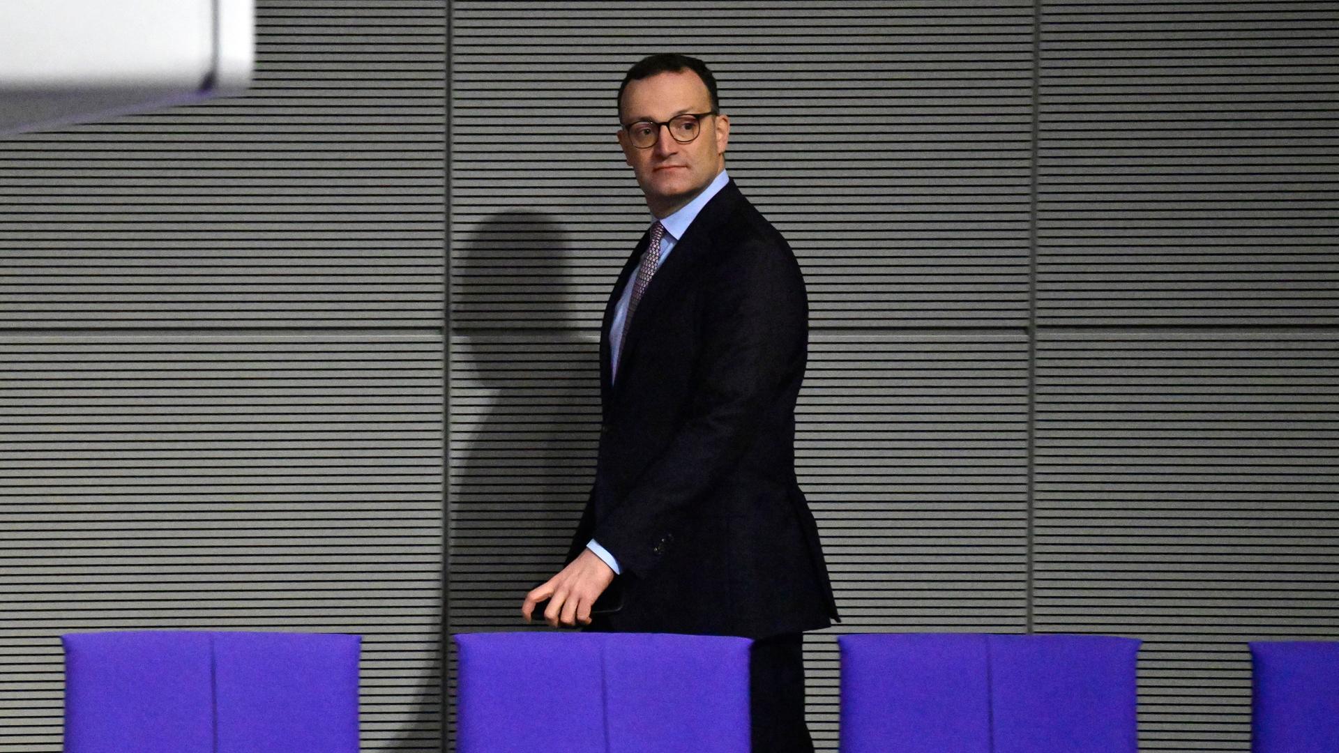 Jens Spahn läuft im Plenarsaal allein hinter einer Stuhlreihe entlang, sein Schatten fällt auf die Wand hinter ihm.
