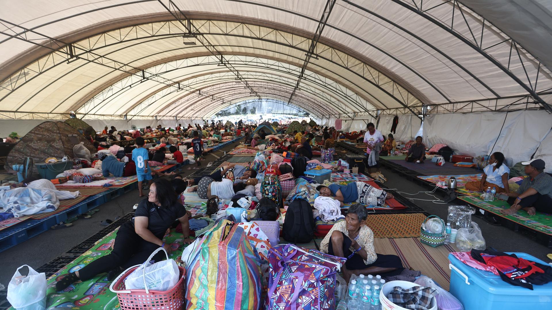 In einem Evakuierungszentrum in der thailändischen Provinz Buriram sitzen und liegen Menschen auf dem Boden und auf einfachen Matten. In einem Evakuierungszentrum in der thailändischen Provinz Buriram sitzen und liegen Menschen auf dem Boden und auf einfachen Matten.
