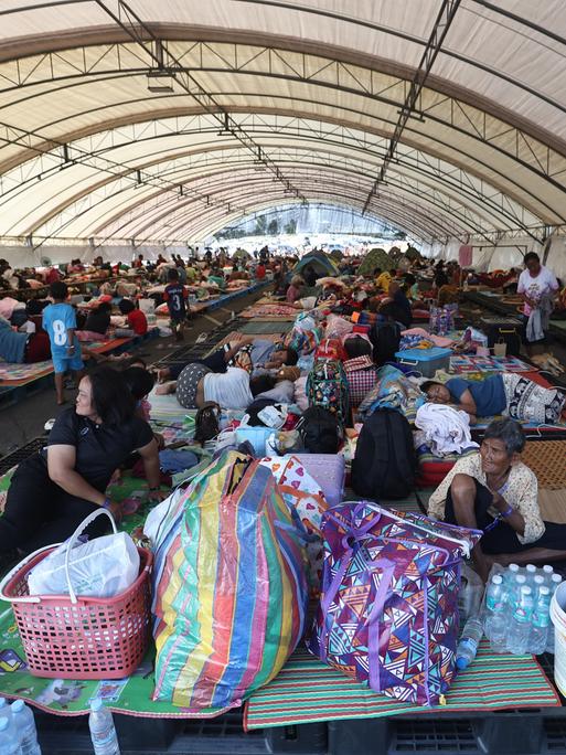 In einem Evakuierungszentrum in der thailändischen Provinz Buriram sitzen und liegen Menschen auf dem Boden und auf einfachen Matten.