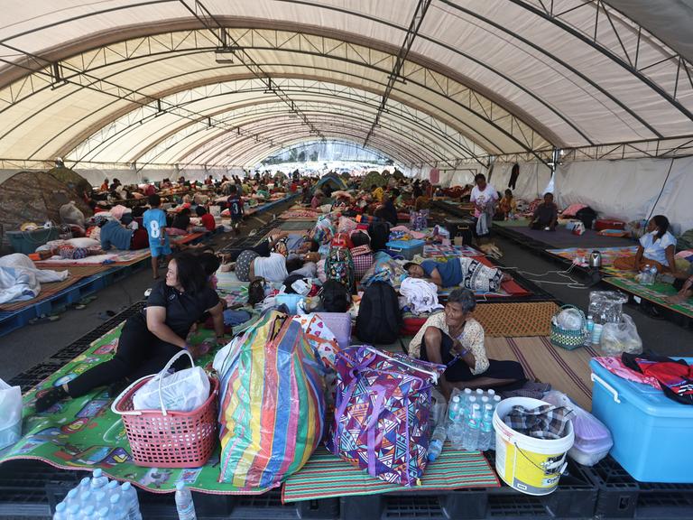 In einem Evakuierungszentrum in der thailändischen Provinz Buriram sitzen und liegen Menschen auf dem Boden und auf einfachen Matten.