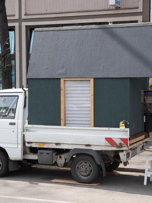 Ein Transporter auf dessen Ladefläche ein kleines Holzhaus steht