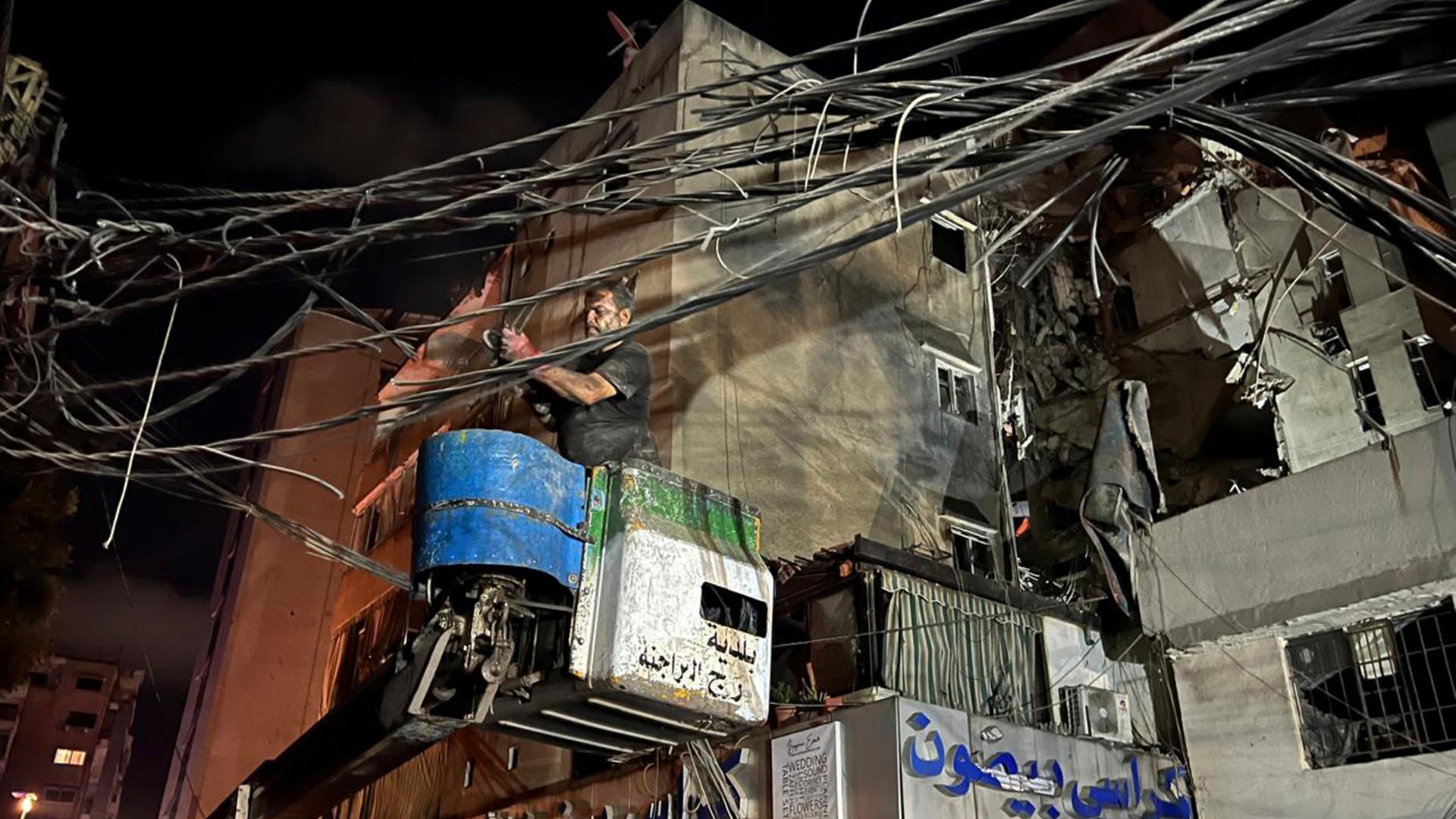 Ein Mann entfernt Stromkabel in der Nähe eines zerstörten Gebäudes.