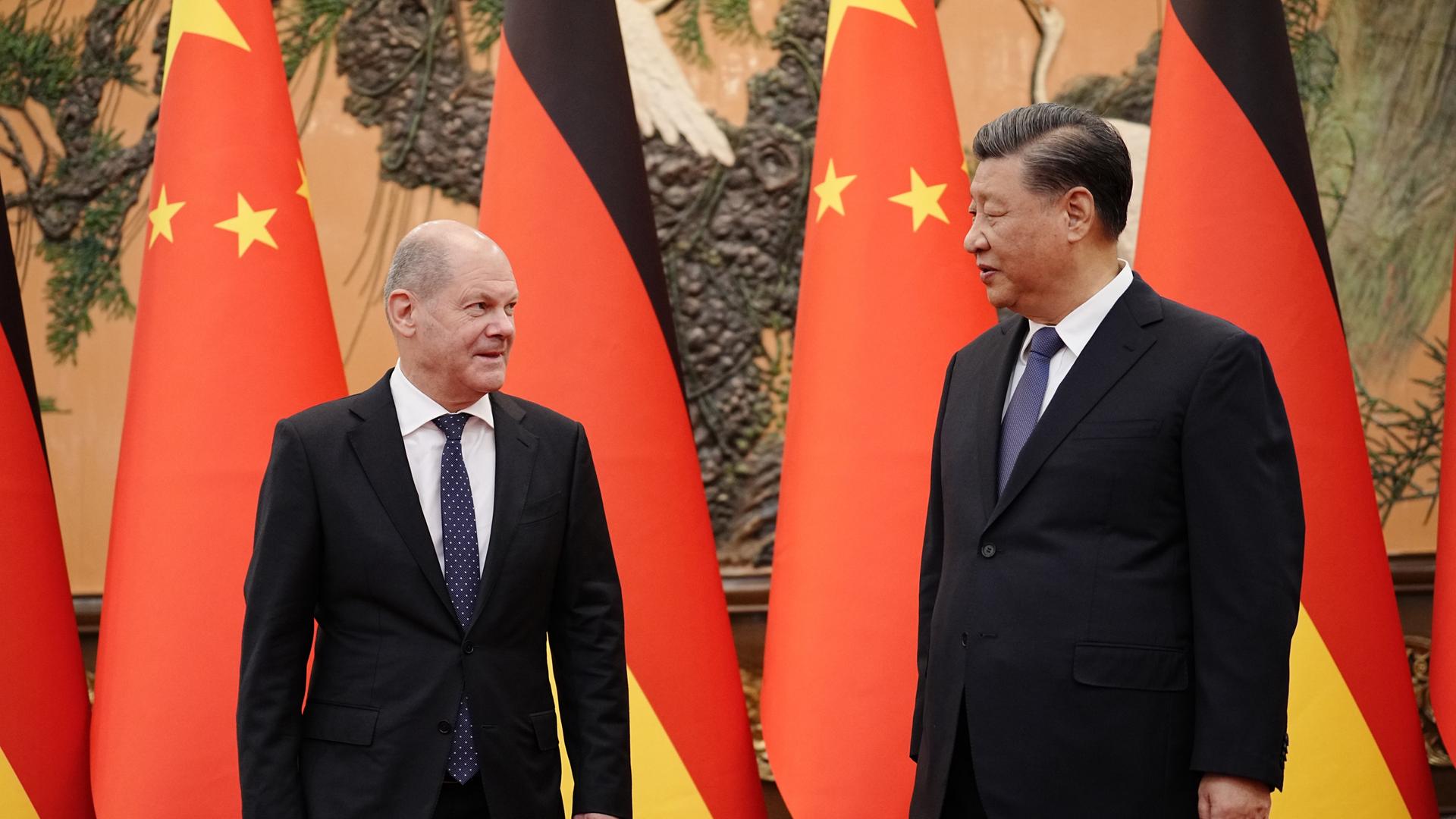 Der chinesische Präsident Xi Jinping (re.) mit Bundeskanzler Olaf Scholz (SPD). Im Hintergrund deutsche und chinesische Fahnen.