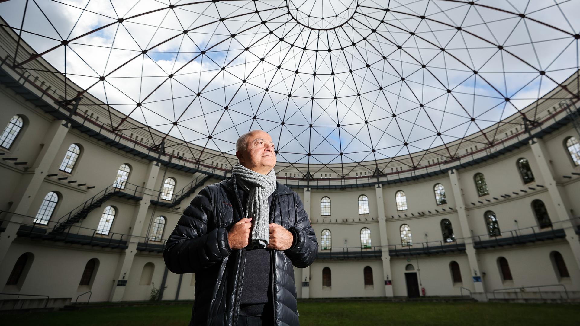 Yadegar Asisi steht in einem für Events genutzten Gasometer und schaut zur runden Glasdecke hoch.