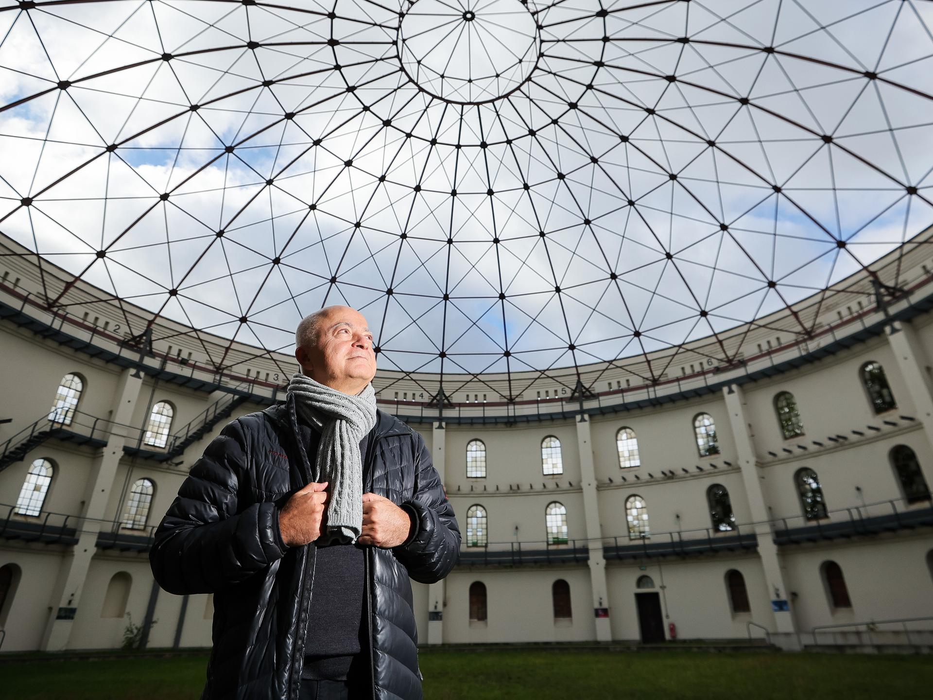 Yadegar Asisi steht in einem für Events genutzten Gasometer und schaut zur runden Glasdecke hoch.