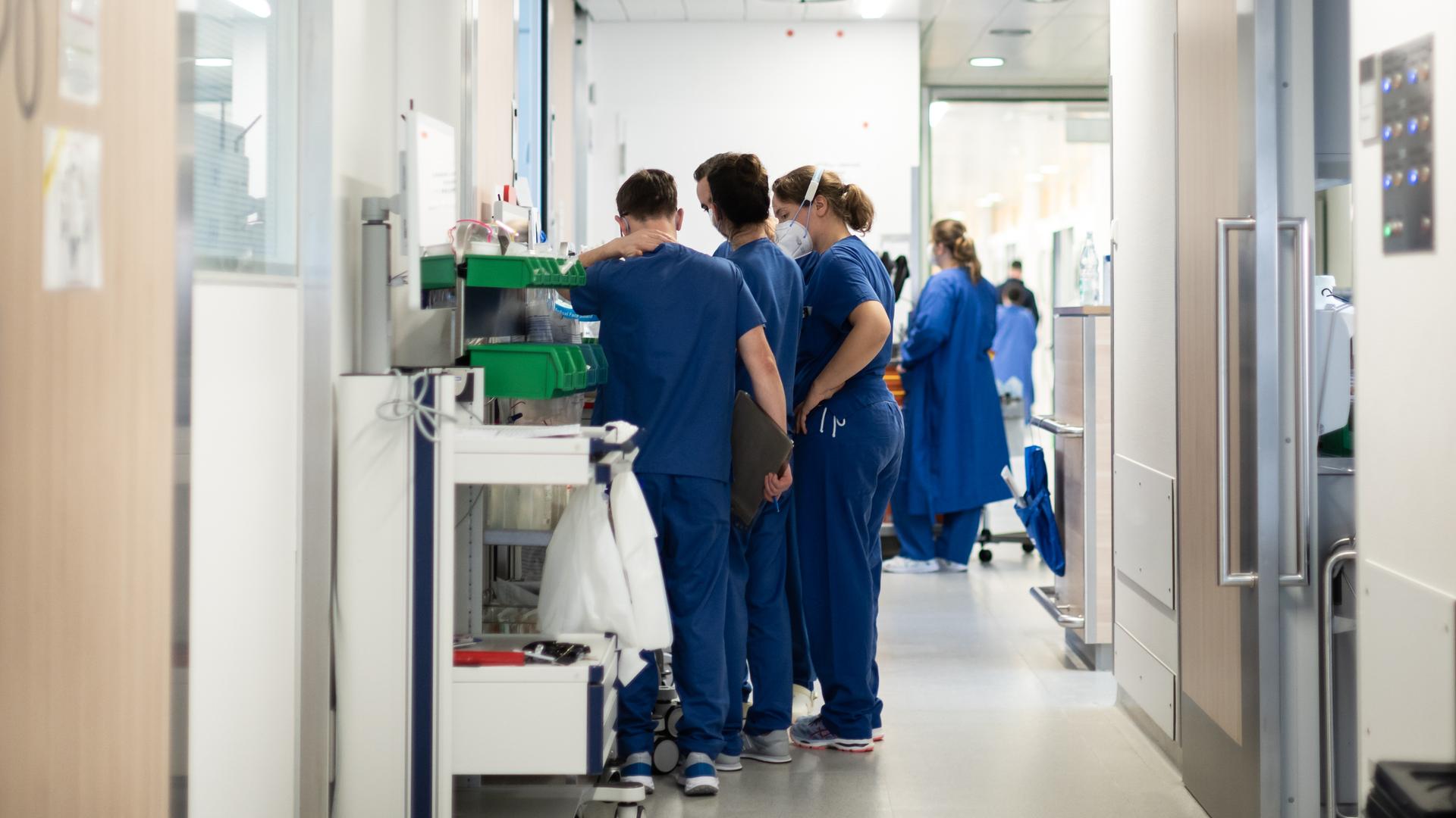 Eine Gruppe von blau-gekleideten Pflegekräften steht auf einem Flur auf der Corona-Intensivstation des Uni Klinikums Essen. Sie tragen FFP2-Masken.