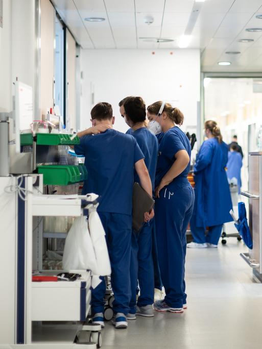 Eine Gruppe von blau-gekleideten Pflegekräften steht auf einem Flur auf der Corona-Intensivstation des Uni Klinikums Essen. Sie tragen FFP2-Masken.