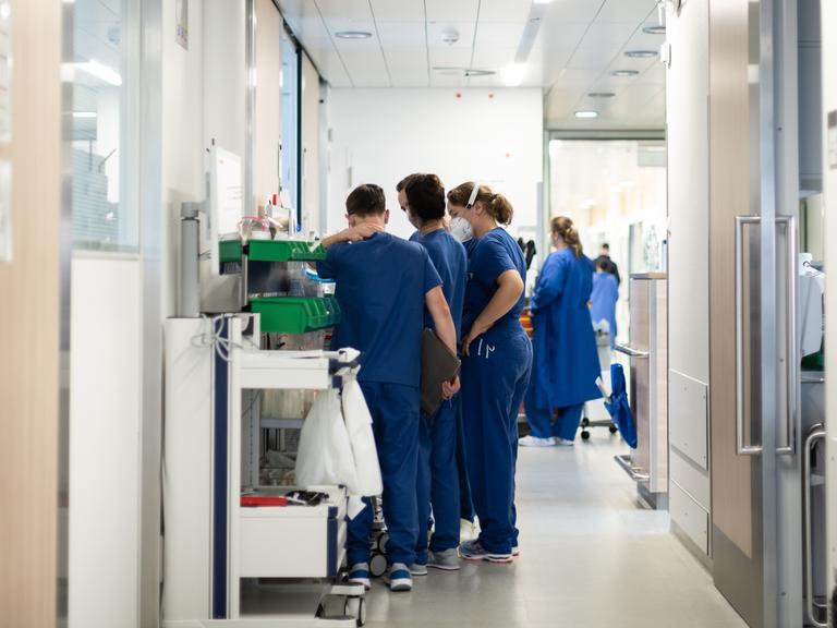 Eine Gruppe von blau-gekleideten Pflegekräften steht auf einem Flur auf der Corona-Intensivstation des Uni Klinikums Essen. Sie tragen FFP2-Masken.