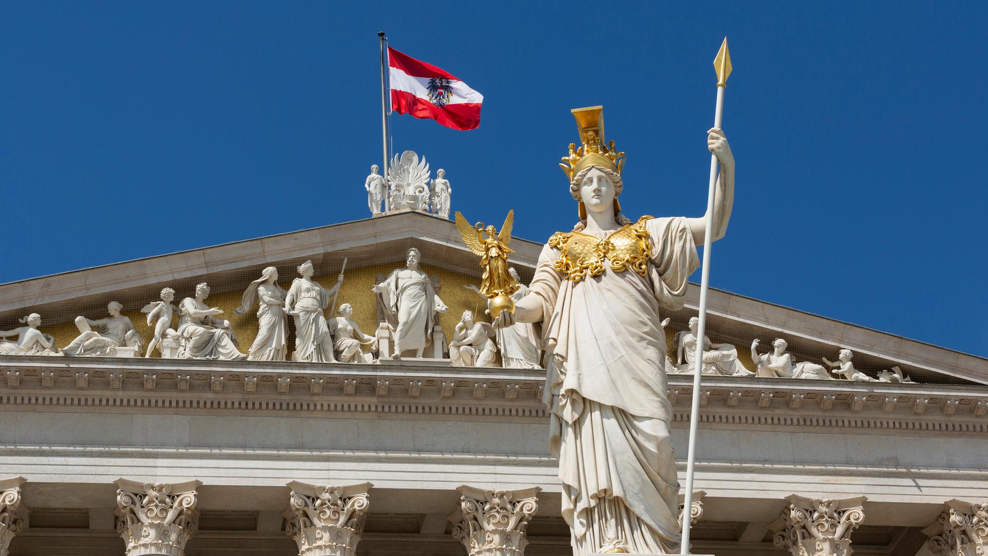 Die Statue der Pallas Athene steht vor dem Parlament in Wien, hinter ihr flattert die österreichische Flagge im Wind.