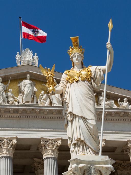 Die Statue der Pallas Athene steht vor dem Parlament in Wien, hinter ihr flattert die österreichische Flagge im Wind.