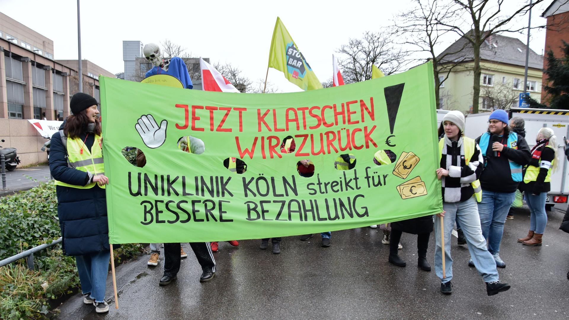Viele Menschen nehmen mit Bannern und Fahnen an einem Warnstreik vor der Uniklinik Köln teil. 