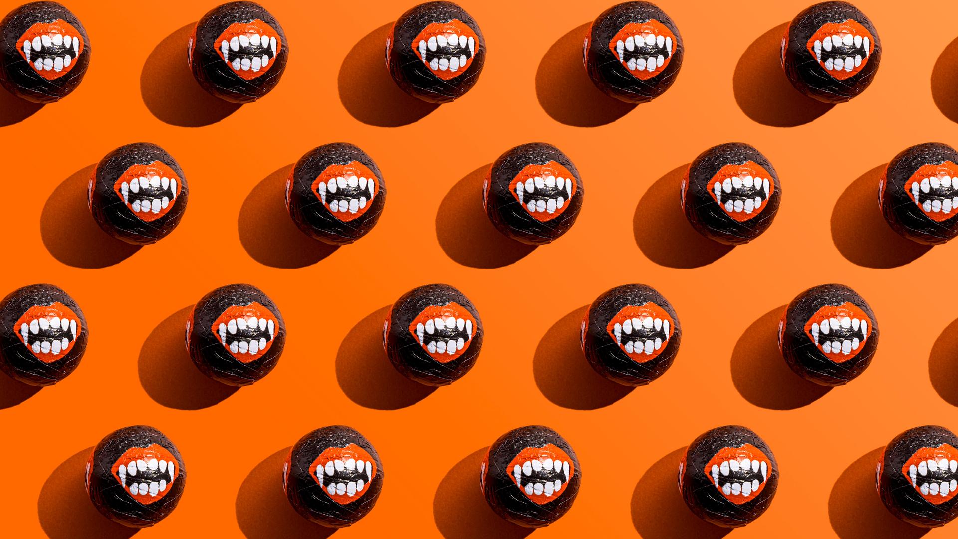 Halloween-Süßigkeiten, deren Umverpackungen Vampirzähne zeigen, liegen aufgereiht vor einem orangefarbenem Hintergrund. Halloween-Süßigkeiten, deren Umverpackungen Vampirzähne zeigen, liegen aufgereiht vor einem orangefarbenem Hintergrund.