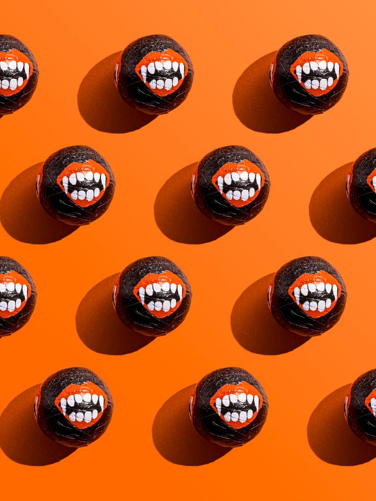 Halloween-Süßigkeiten, deren Umverpackungen Vampirzähne zeigen, liegen aufgereiht vor einem orangefarbenem Hintergrund.