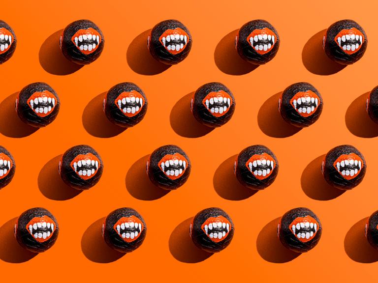 Halloween-Süßigkeiten, deren Umverpackungen Vampirzähne zeigen, liegen aufgereiht vor einem orangefarbenem Hintergrund.