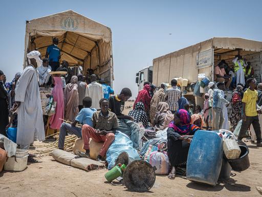 Menschen im Sudan in traditioneller Kleidung sitzen vor zwei LKW und scheinen zu warten