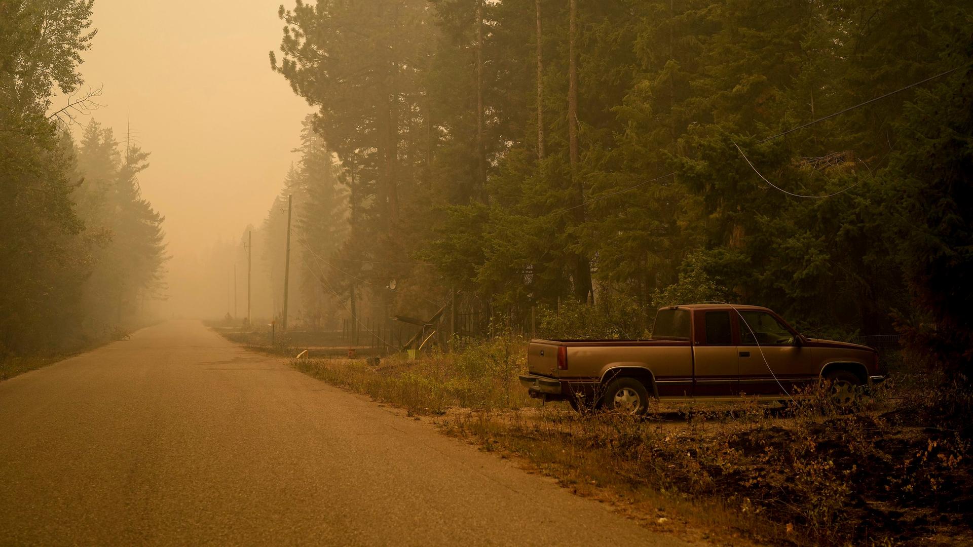 Auf einer Straße, die durch und einen Wald führt, steht ein verlassener Pickup. Die Luft ist voller Rauch und Qualm.