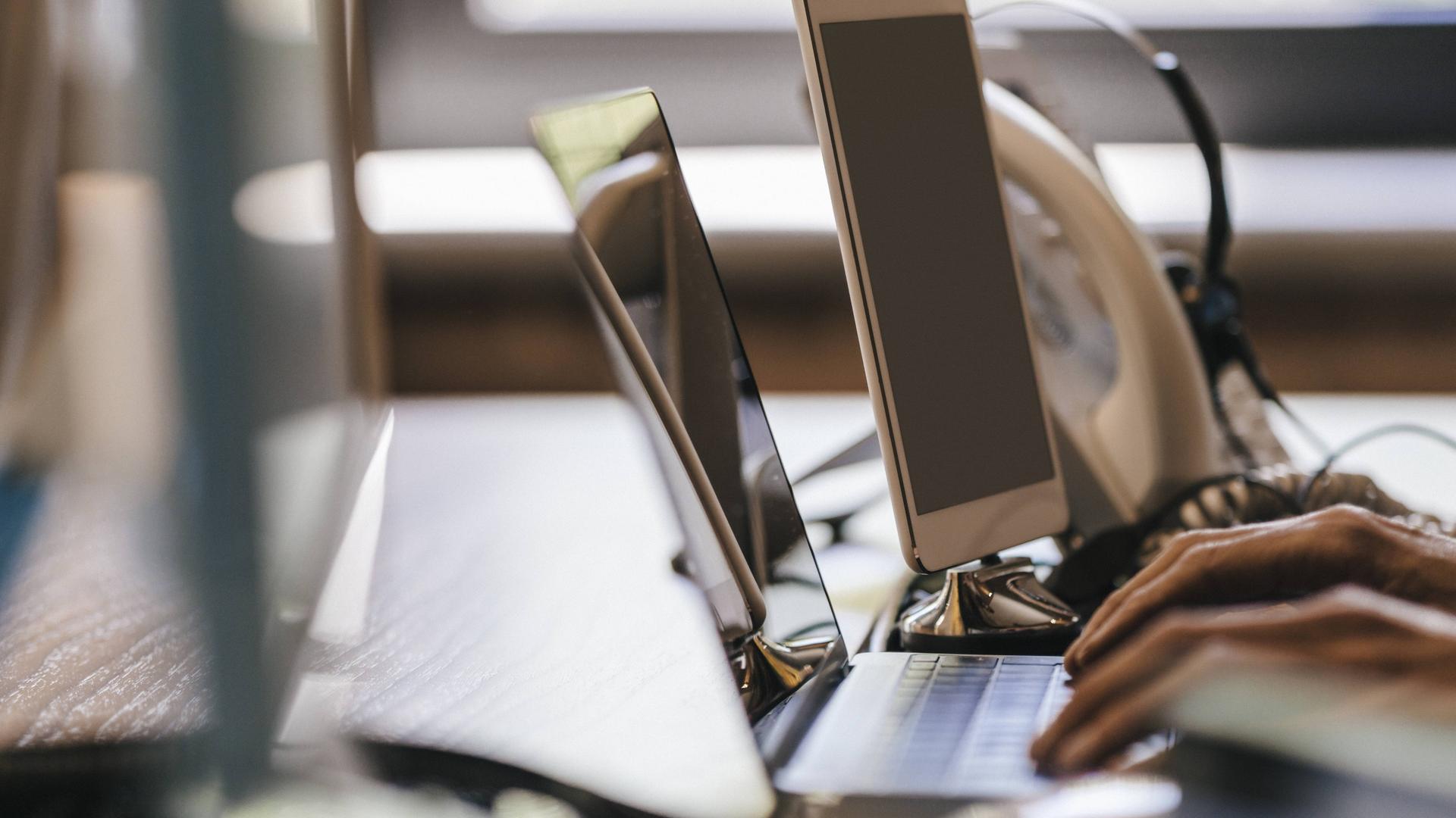 Arbeitssetting mit Telefon und Händen auf dem Laptop.
