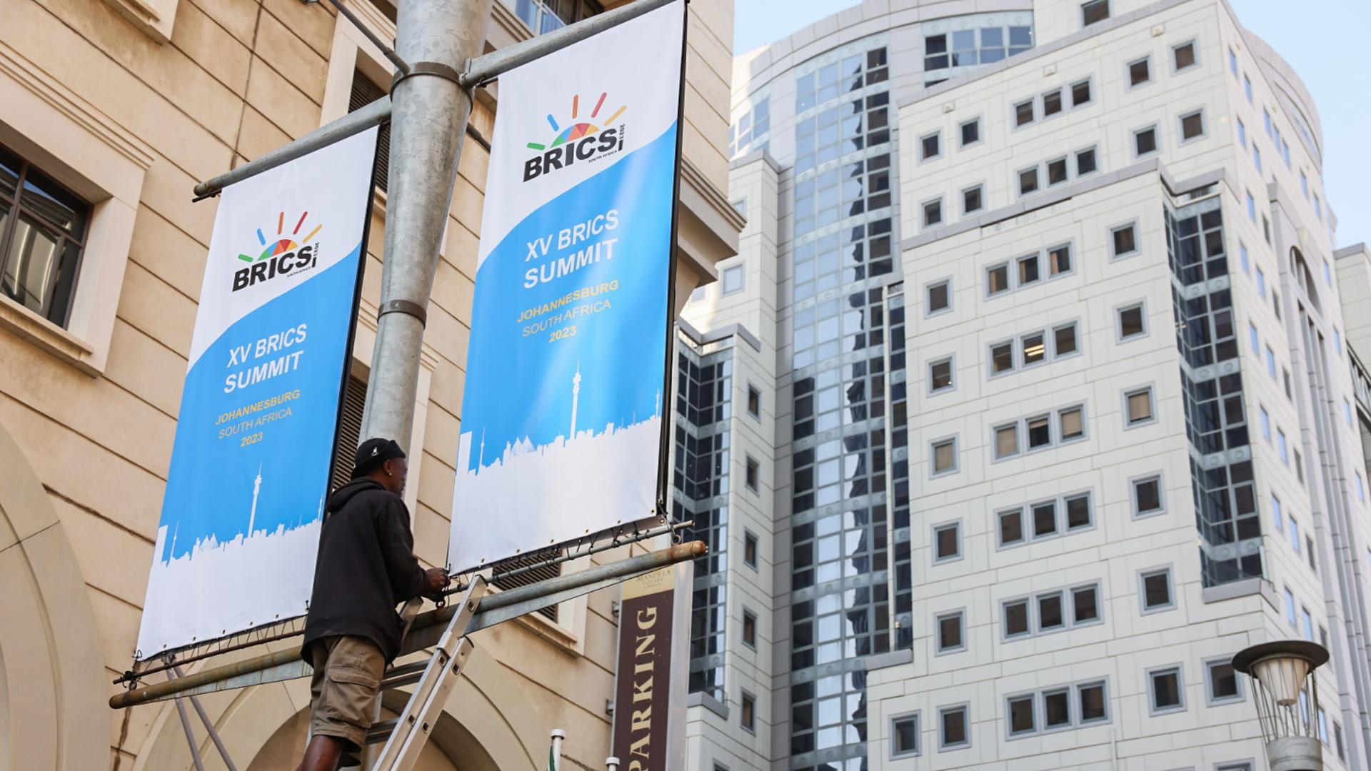 Ein Mann hängt Werbebanner für den BRICS-Gipfel in Johannesburg auf. 