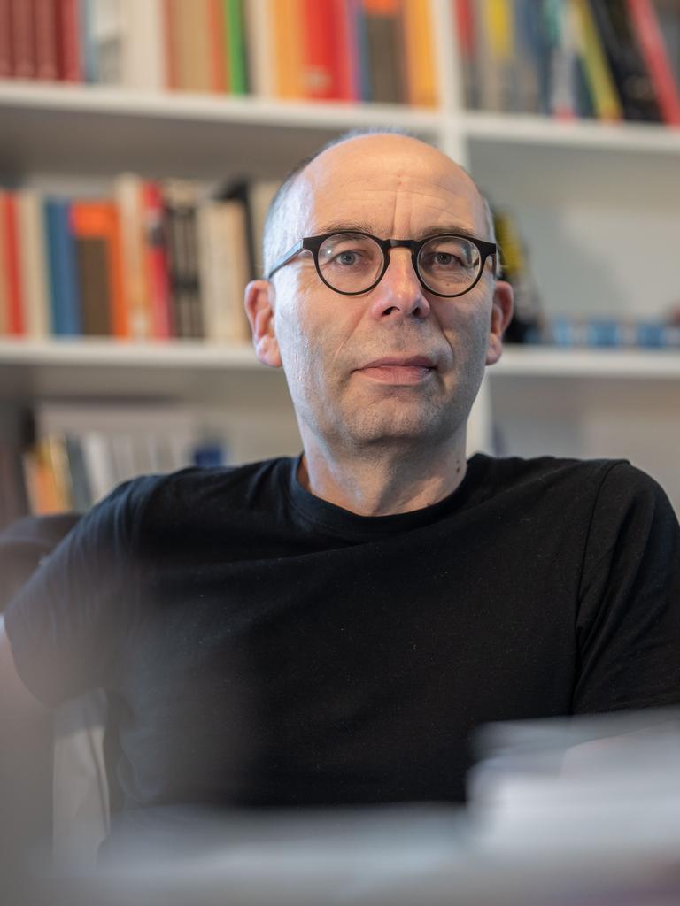 Der Soziologe Stephan Lessenich sitzt in einem schwarzen T-Shirt an seinem Schreibtisch vor einem Bücherregal.
