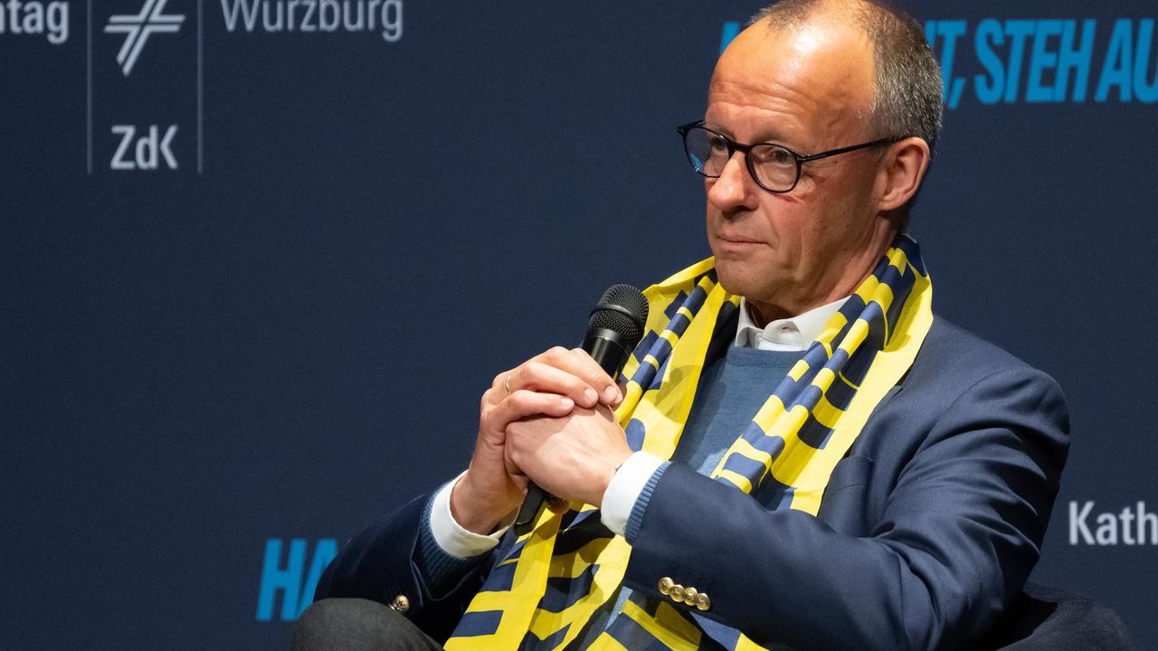 Bundeskanzler Merz sitzt mit einem Mikrofon in der Hand auf der Bühne des Deutschen Katholikentags in Würzburg.