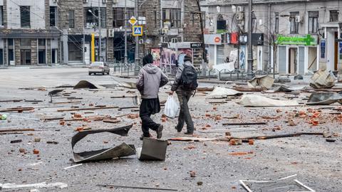 Zwei Männer laufen in Charkiw über Trümmerteile auf der Straße nach dem Beschuss durch russische Truppen.