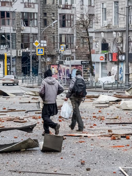 Zwei Männer laufen in Charkiw über Trümmerteile auf der Straße nach dem Beschuss durch russische Truppen.