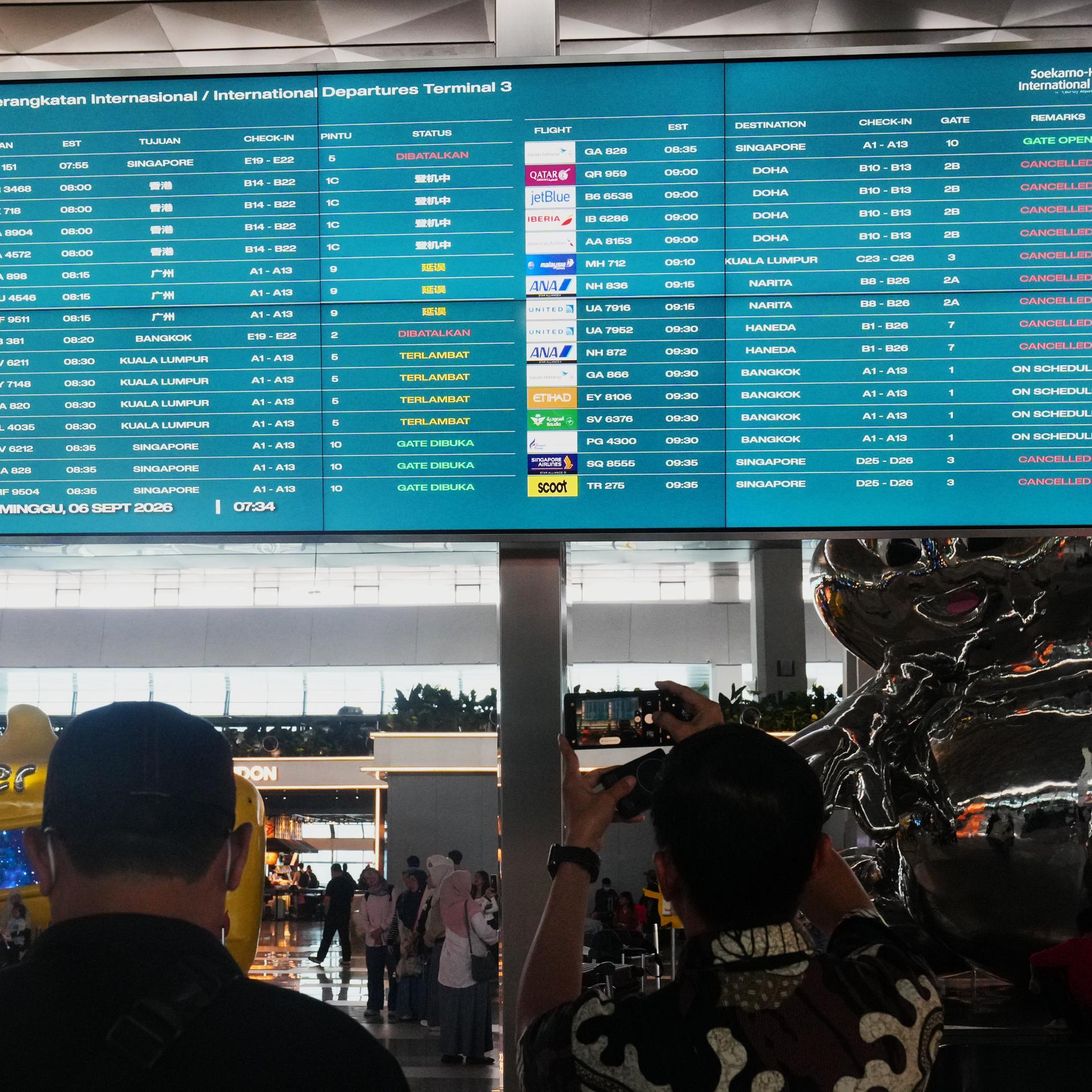 Reisende gehen im indonesischen Hauptstadtflughafen Soekarno-Hatta an einer Informationstafel vorbei, auf der Flugausfälle angezeigt werden. 