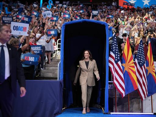 Die demokratische Präsidentschaftskandidatin und US-Vizepräsidentin Kamala Harris geht durch ein blaues Tor bei einer Wahlkampfveranstaltung in Glendale, Arizona. Um sie herum Fahnen und Fans, 9. August 2024.