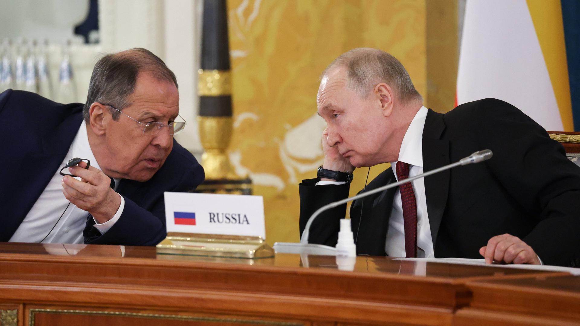 Russlands Präsident Putin und der russische Außenminister Lawrow im Gespräch bei einer Konferenz. Zwischen ihnen steht ein Schild auf dem Tisch mit der Aufschrift "Russia"