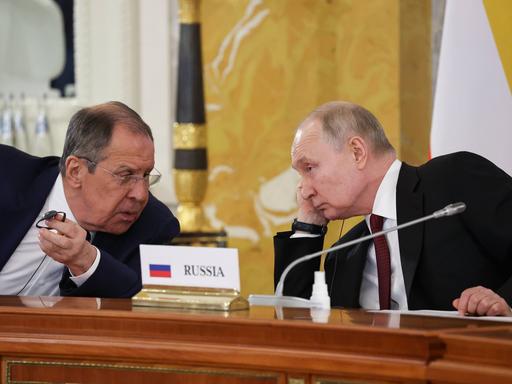 Russlands Präsident Putin und der russische Außenminister Lawrow im Gespräch bei einer Konferenz. Zwischen ihnen steht ein Schild auf dem Tisch mit der Aufschrift "Russia"