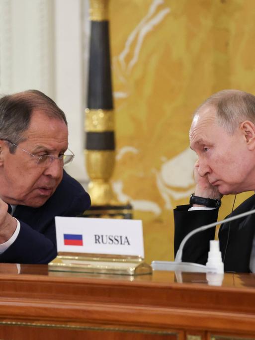 Russlands Präsident Putin und der russische Außenminister Lawrow im Gespräch bei einer Konferenz. Zwischen ihnen steht ein Schild auf dem Tisch mit der Aufschrift "Russia"
