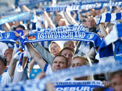 Fans des Vereins FC Magdeburg halten Schals in die Höhe mit der Aufschrift "Ostdeutschland".
