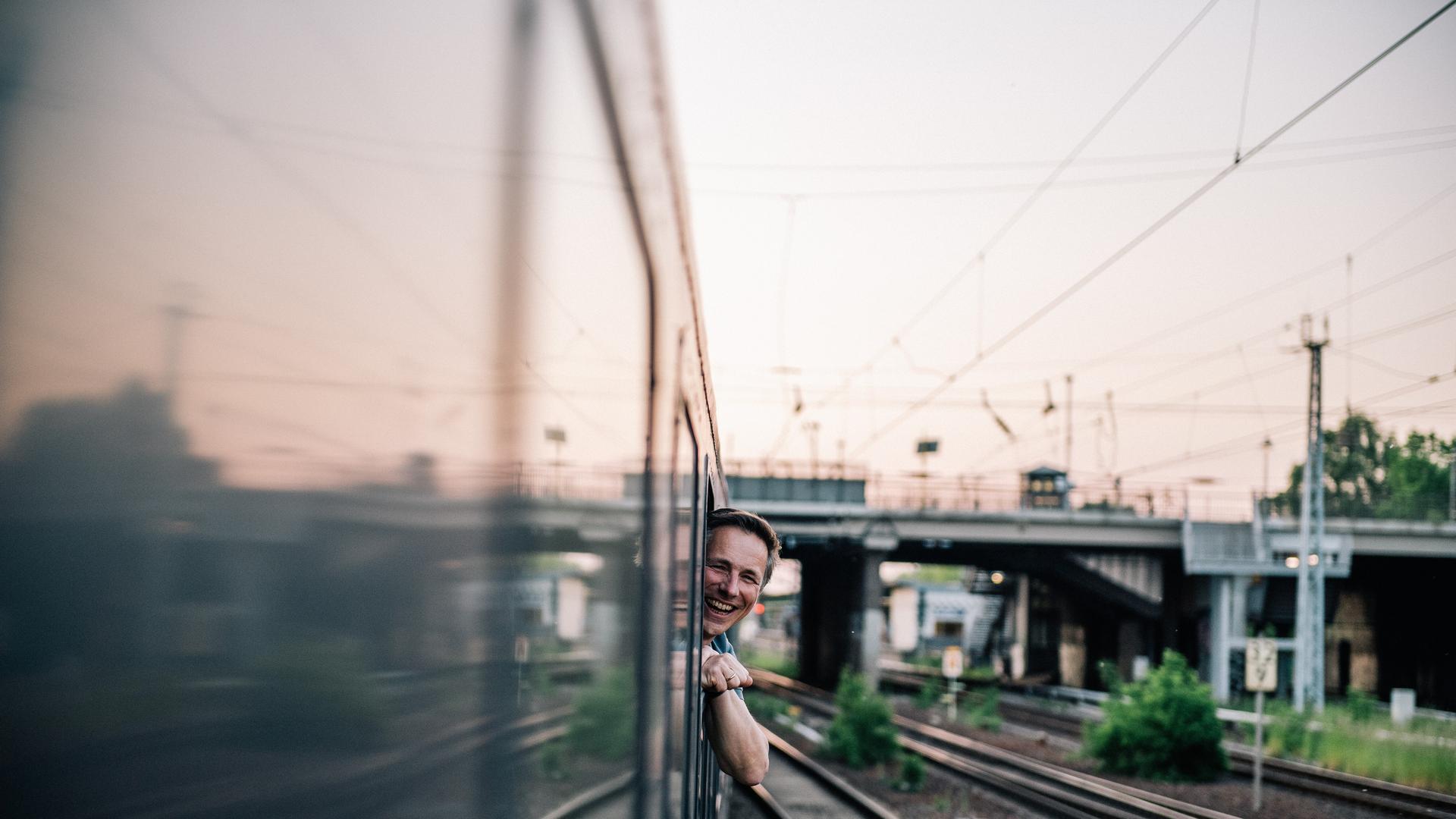Ein Mann lehnt sich lächelnd aus einem Zugfenster