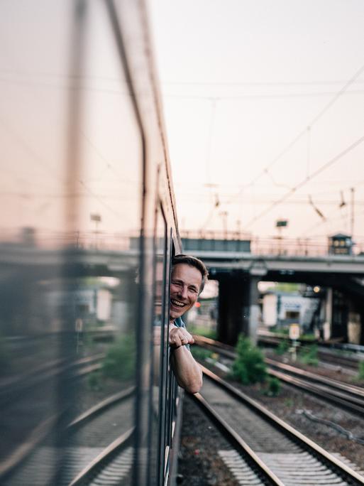 Ein Mann lehnt sich lächelnd aus einem Zugfenster
