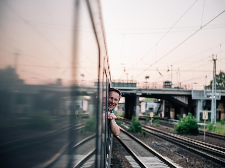 Ein Mann lehnt sich lächelnd aus einem Zugfenster