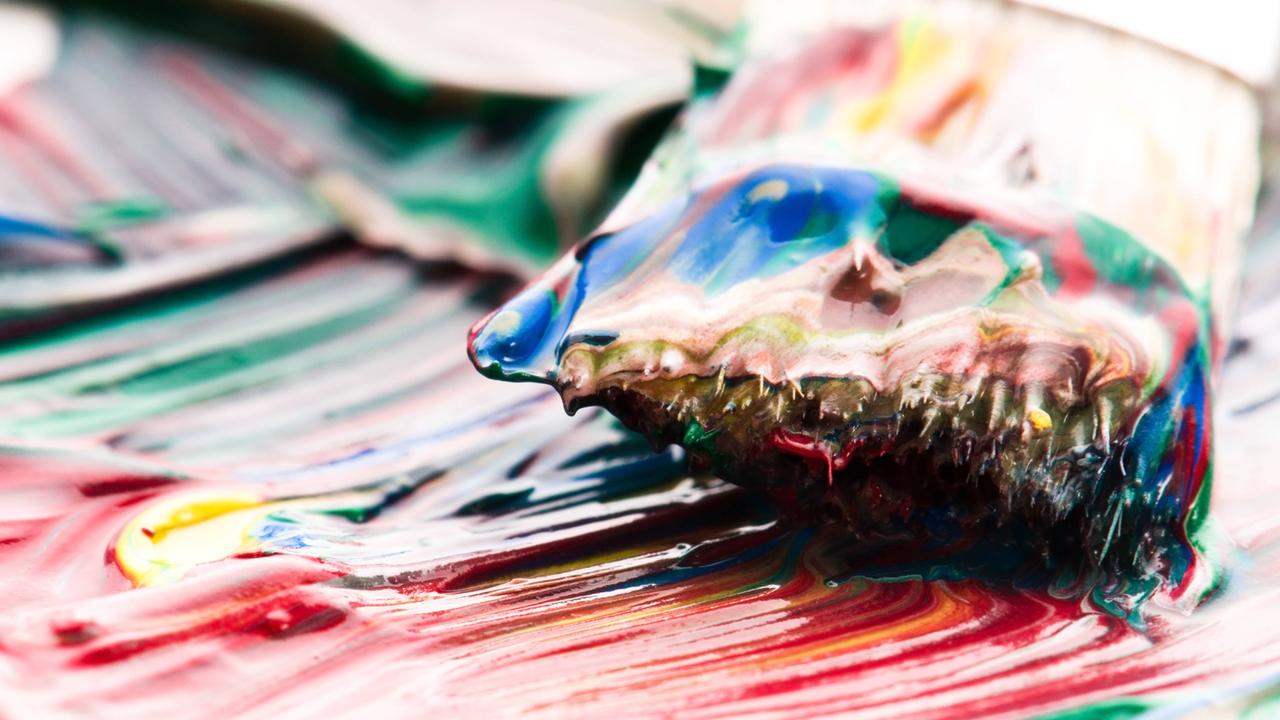 Ein Pinsel mischt bunte Ölfarben auf einer Palette.