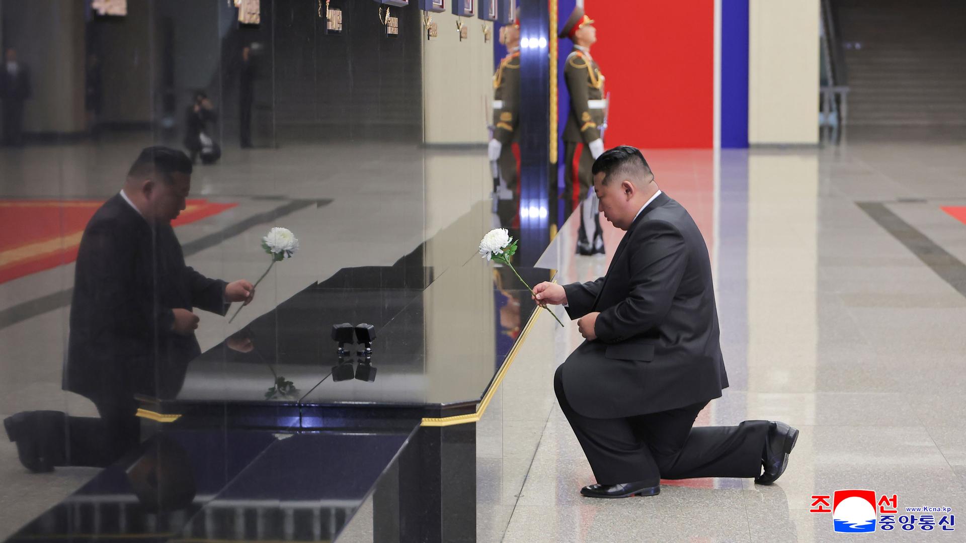 Kim Jong Un kniet vor einer Wand mit Fotos von getöteten Soldaten. In der Hand hält er eine Blume. Kim Jong Un kniet vor einer Wand mit Fotos von getöteten Soldaten. In der Hand hält er eine Blume.