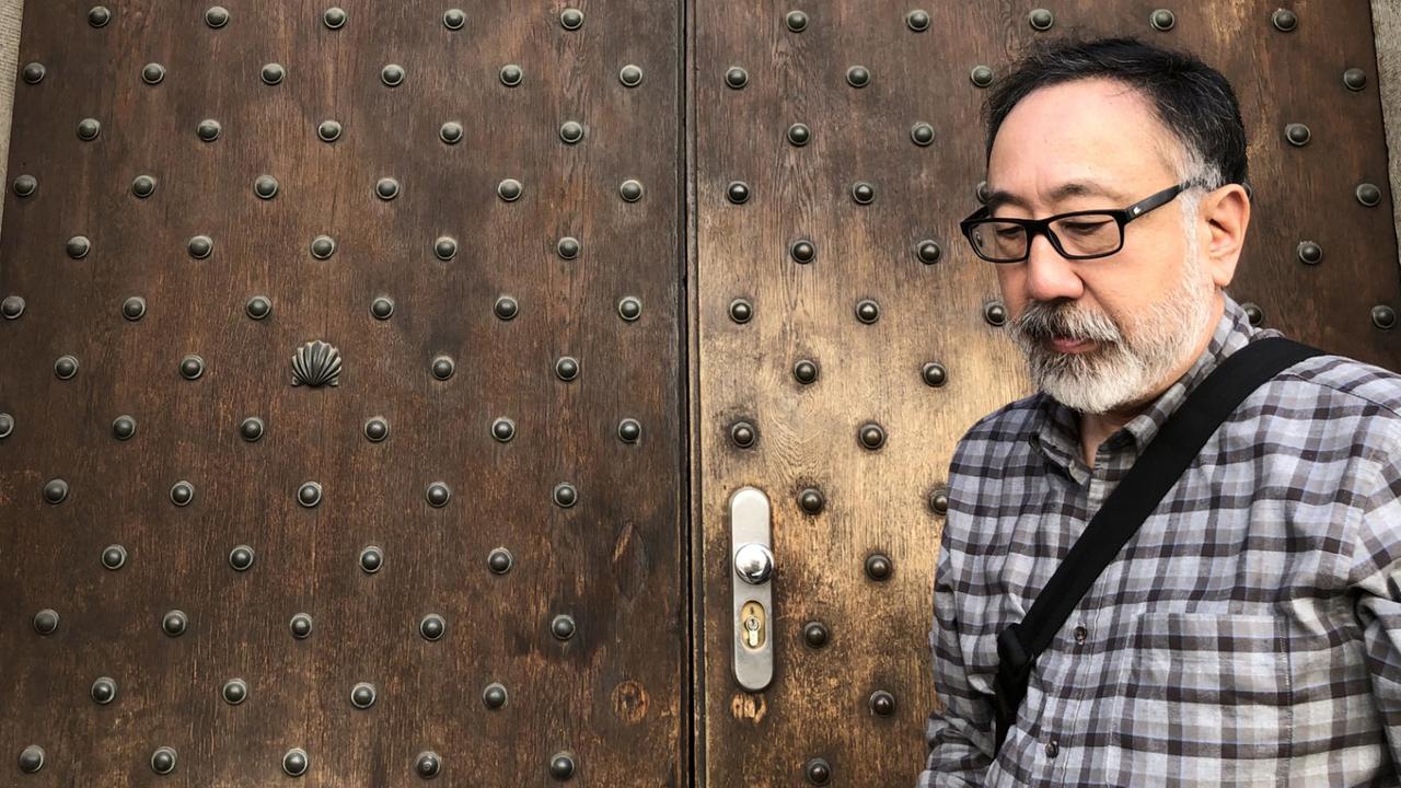 Ein Mann mit Brille und karriertem Hemd steht vor einer sehr alten Holztür mit neuem provisorischem Beschlag
