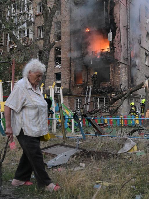 Ukraine, Kiew: Eine Frau geht nach einem russischen Angriff an einem brennenden Wohnhaus vorbei. 