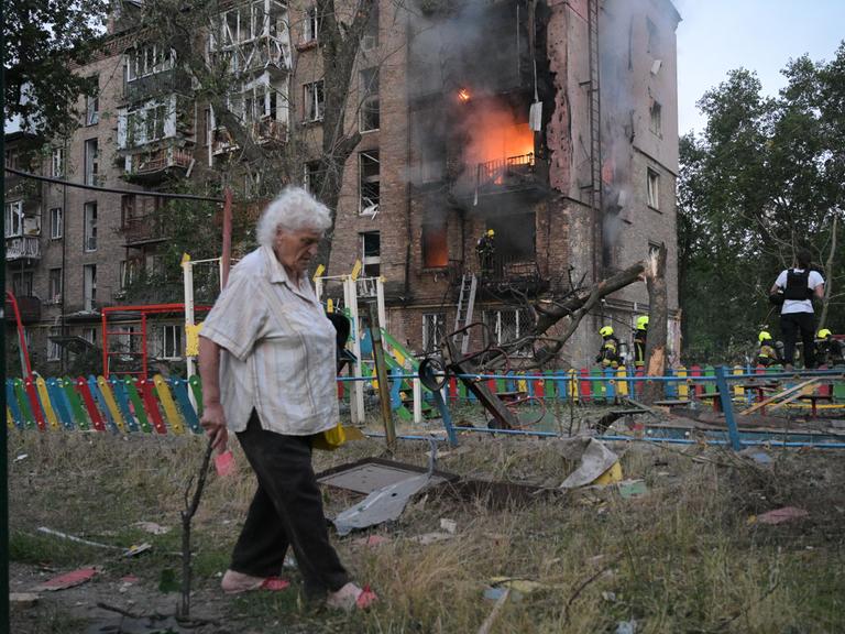 Ukraine, Kiew: Eine Frau geht nach einem russischen Angriff an einem brennenden Wohnhaus vorbei. 