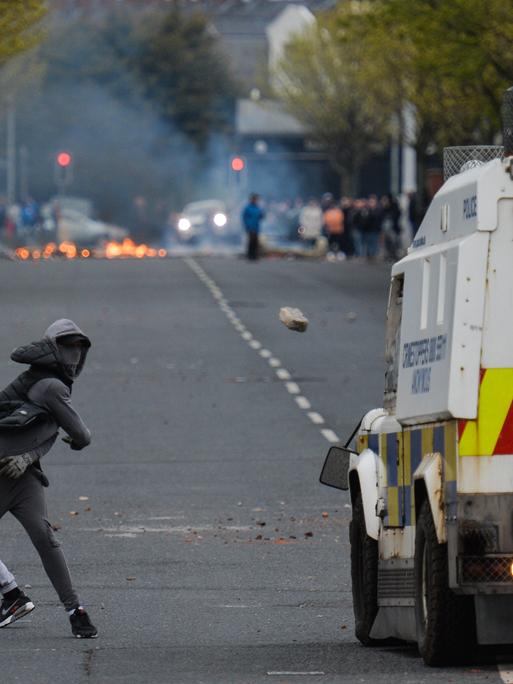 Ein vermummter junger Mann wirft einen Stein auf ein Polizeiauto bei Protesten im April 2021 in Belfast.