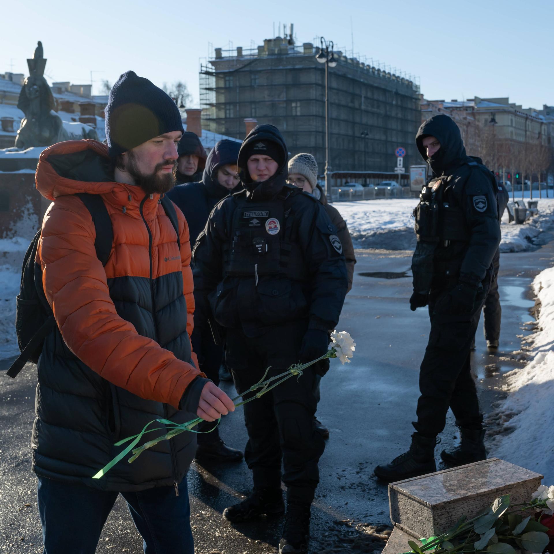 Polzisten beobachten einen Mann der am 16. Februar 2025 Blumen am Mahnmal für die Opfer politischer Repressalien in St. Petersburg niederlegt.